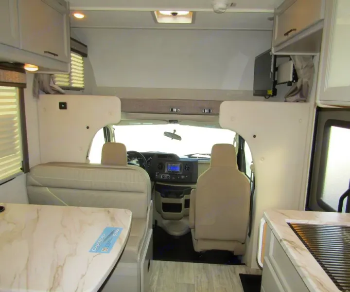 RV rental interior: front view of cab, overhead bunk, dinette, and kitchen area with light decor. Perfect for road trips.. Thor Chateau 2025