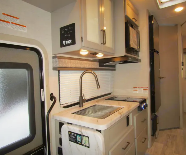RV rental's compact kitchen: sleek sink, stovetop, microwave, and cabinets, with a fridge on the right. Enjoy meals on the go.. Thor Chateau 2025