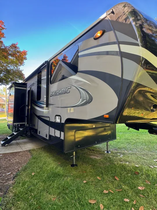 A large, modern Seismic fifth-wheel RV rental is parked on grass with its entrance steps extended, ideal for travel.. Jayco Seismic 2016