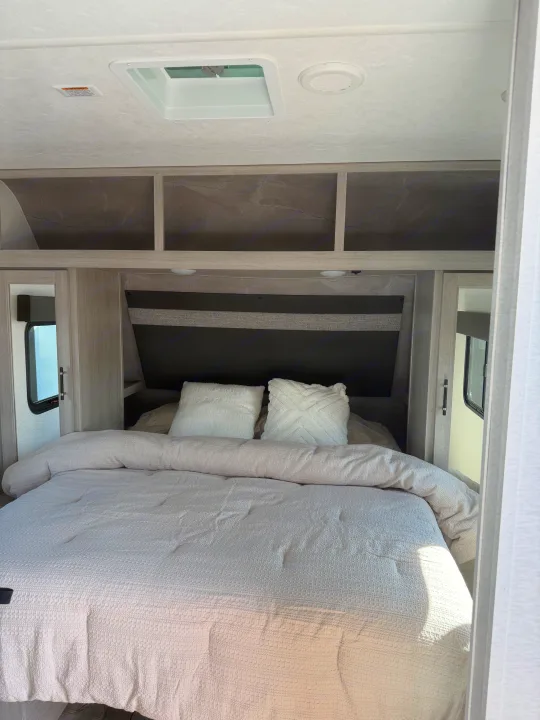 Modern RV rental bedroom with white bedding, overhead storage, and ceiling vents. Cozy camper interior designed for comfort.. Crossroads RV Sunset Trail Sport 2025
