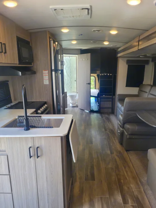 Modern rv rental interior featuring a kitchen with sink, stove, and microwave, plus a dining area, bathroom, and bunk beds.. Keystone RV Passport GT 2022