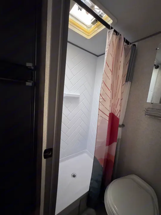 RV rental bathroom features: a white herringbone shower, overhead skylight, and a toilet, highlighting compact design.. Forest River Salem FSX 2020