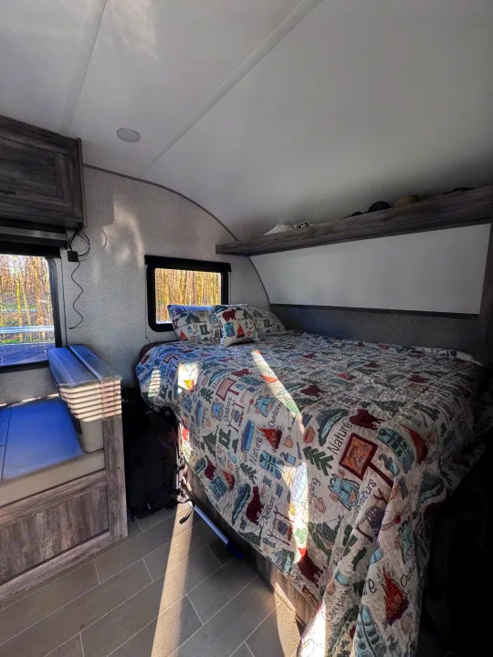 Cozy RV rental interior: bedroom with nature-themed bedding, windows with outdoor views, and a bench seating area.. Forest River Salem FSX 2020