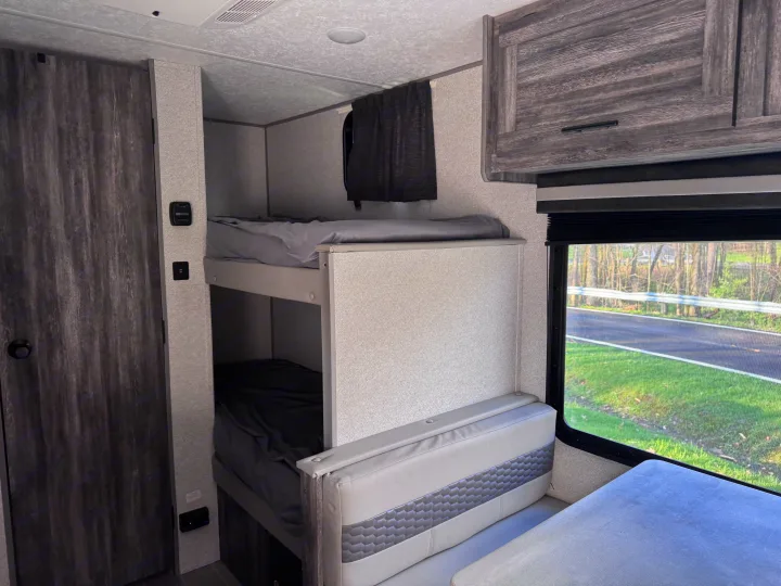 Cozy RV rental interior showing bunk beds with grey bedding, a dinette, and a window overlooking a road.. Forest River Salem FSX 2020
