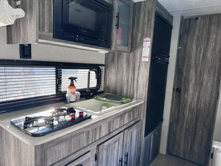 Modern RV rental kitchen featuring a compact stove, sink, microwave, and refrigerator, ideal for road trips.. Forest River Salem FSX 2020