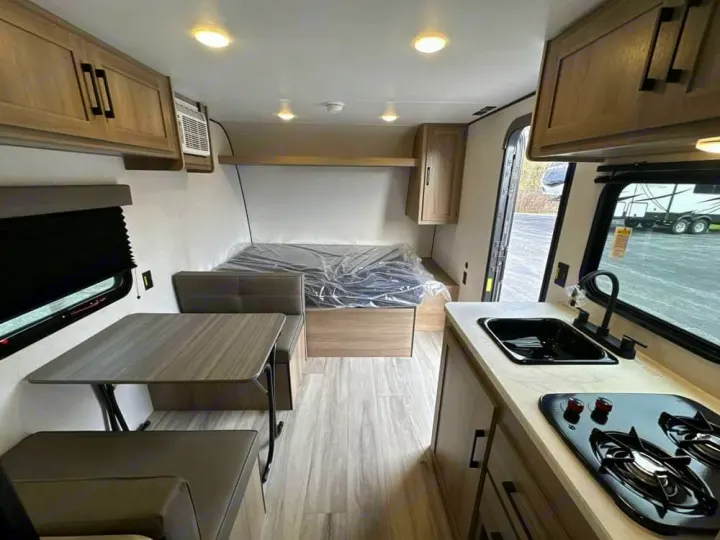 View inside an RV rental, featuring a compact kitchen with stove and sink, dinette, and rear bed with plastic cover.. Coleman Coleman 17B 2026