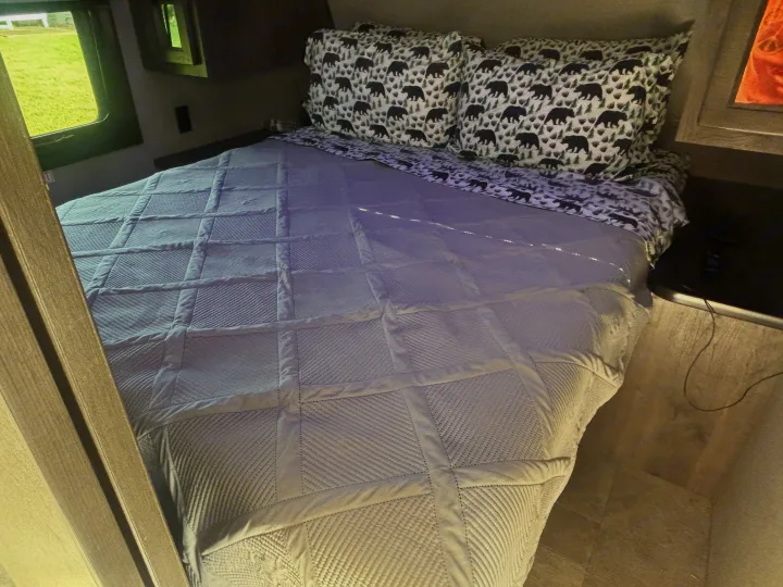 Cozy bed in an RV rental, featuring bear-patterned pillows, a quilted blanket, and a view of green outside.. Jayco Jay Flight 2020