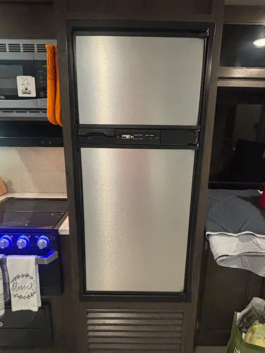 RV rental kitchen: a compact space with a two-door fridge, microwave (with Sasquatch sticker), and stove with blue knobs.. Jayco Jay Flight 2020