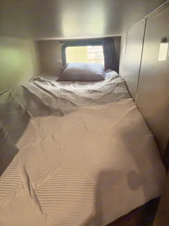 RV rental interior: a neatly made bed with grey quilt and pillow, ready for rest. An 'EXIT' sign is visible by the window.. Jayco Jay Flight 2020