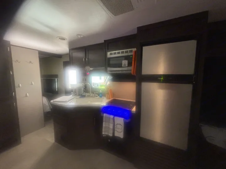 Compact rv rental kitchen features dark cabinets, fridge, microwave, sink, and stove with blue lights. Ideal for travel.. Jayco Jay Flight 2020