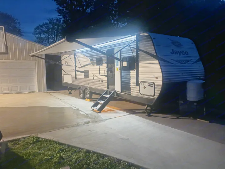 A brightly lit Jayco travel trailer RV rental is parked at night with its awning extended on a concrete driveway.. Jayco Jay Flight 2020