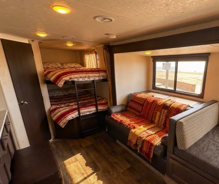 This RV rental features comfy bunk beds, a cozy couch with vibrant blankets, and a window view of a sunny beach.. Forest River Salem Cruise Lite 2019