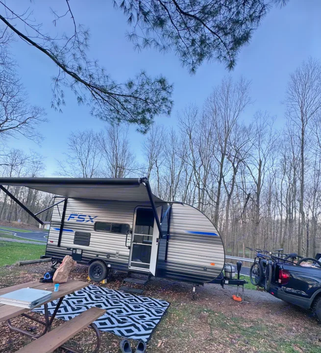 Our RV rental campsite ready! Travel trailer, truck with bikes, picnic table, and awning extended under a clear sky for outdoor adventures.. Forest River Salem FSX 2020