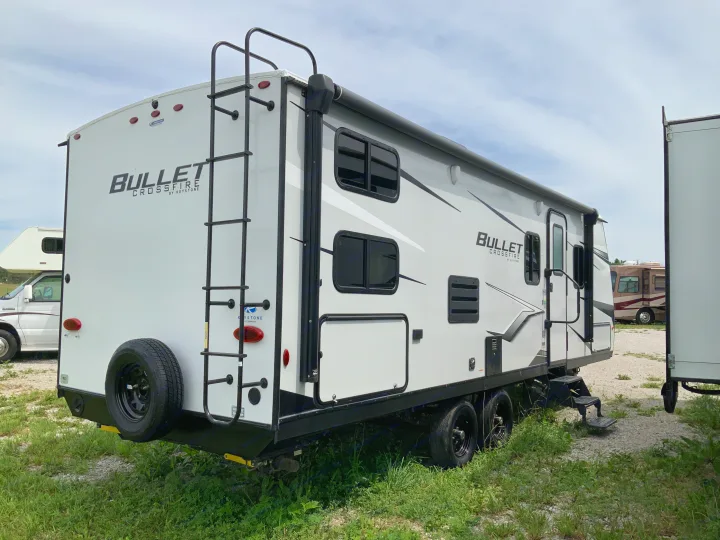 This white Keystone Bullet Crossfire travel trailer, a great rv rental option, features a rear ladder, spare tire, and side awning.. Keystone RV Bullet Crossfire 2022