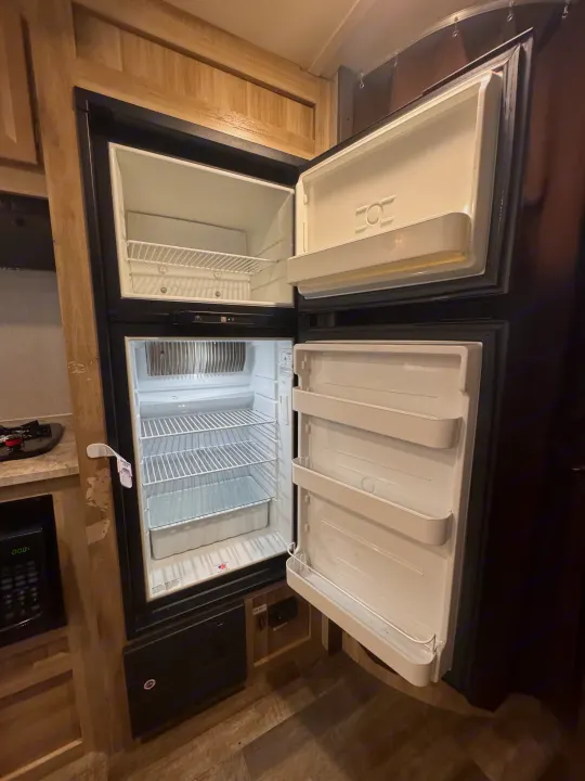Explore this RV rental's kitchen! An open, empty refrigerator features a top freezer and lower fridge, ready for food.. Coachmen 184BHS 2021