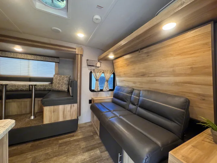 RV rental interior: A cozy living space with a dinette, sofa, wood-look walls & floors, and bright overhead lighting.. Coachmen 184BHS 2021