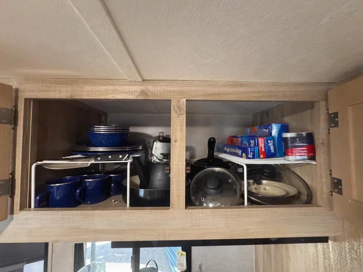Organized **rv rental** kitchen cabinet with blue enamel dishes, pots, Ziploc bags, Reynolds Wrap, and salt container.. Coachmen 184BHS 2021