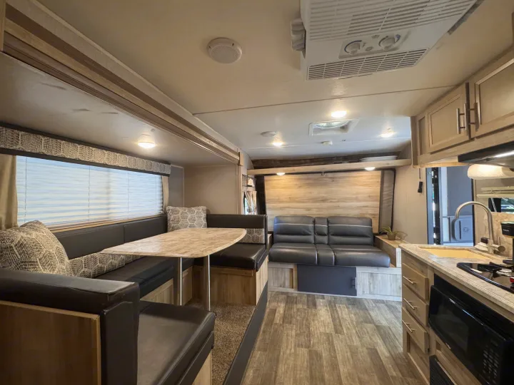 This cozy RV rental interior features a dining booth, comfortable sofa/sleeping area, and a compact kitchen for your adventures.. Coachmen 184BHS 2021