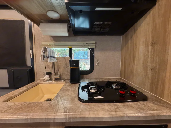 Compact RV rental kitchen featuring a sink, two-burner stove, coffee maker, and paper towel holder, perfect for travel.. Coachmen 184BHS 2021