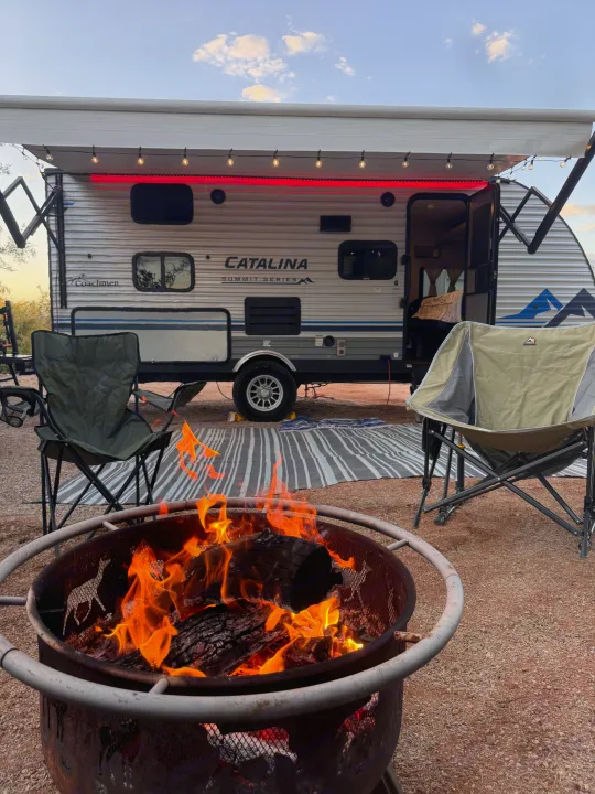 Relaxing RV rental evening: A cozy campsite features a travel trailer with string lights, camping chairs, and a warm fire pit with deer cutouts.. Coachmen 184BHS 2021