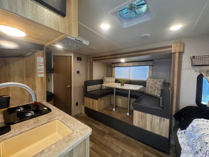 Modern RV rental interior with a light wood-themed kitchen and U-shaped dinette seating, ready for adventure.. Coachmen 184BHS 2021