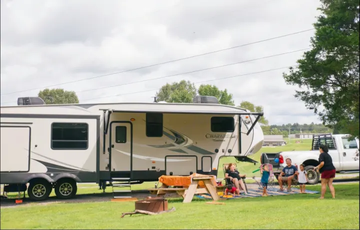 Family enjoys an RV rental vacation. Adults relax, kids play by the Coachmen Chaparral fifth wheel at their campsite.. Coachmen Chaparral 2018