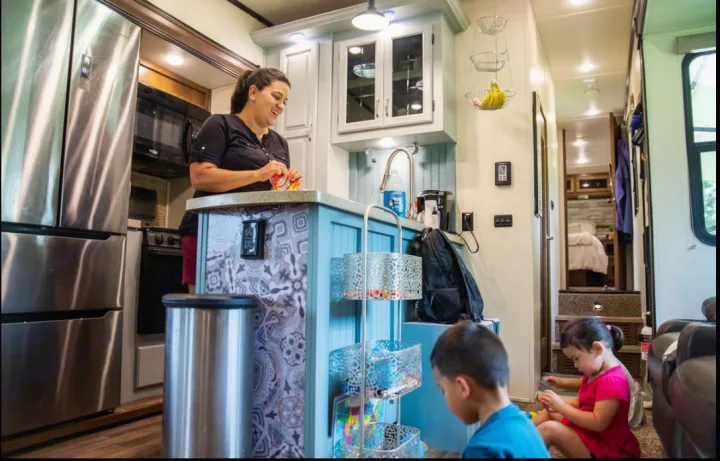 Family fun in an RV rental: A woman preps snacks in the compact kitchen as two children play on the floor.. Coachmen Chaparral 2018