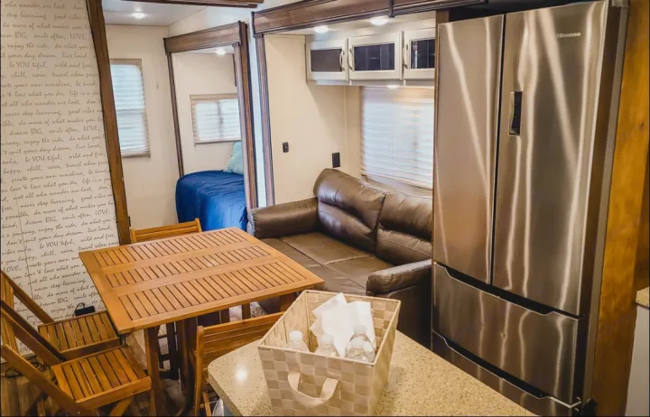 RV rental with modern living space: Hisense fridge, sofa, wooden dining table, and a peek into the bedroom.. Coachmen Chaparral 2018