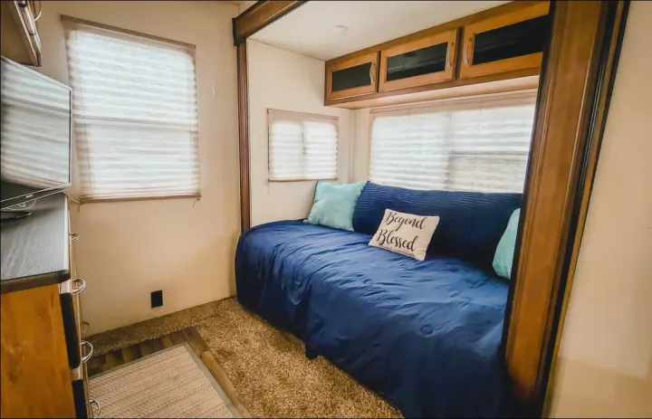 Enjoy this cozy RV rental bedroom/lounge with a comfy blue daybed, windows, TV, & storage cabinets.. Coachmen Chaparral 2018