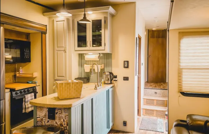 Bright, full kitchen with counter, sink, stove, microwave, and cabinets in an RV rental, plus a hallway with stairs.. Coachmen Chaparral 2018