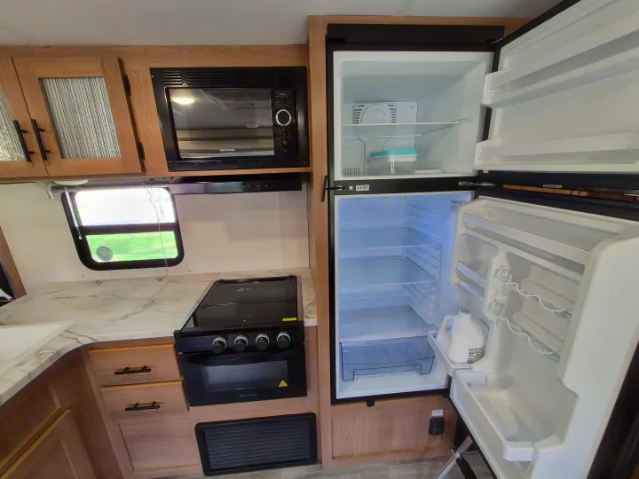 Clean RV rental kitchen showing microwave, stove, and open refrigerator, ideal for travel accommodations.. Avenger LE 2022