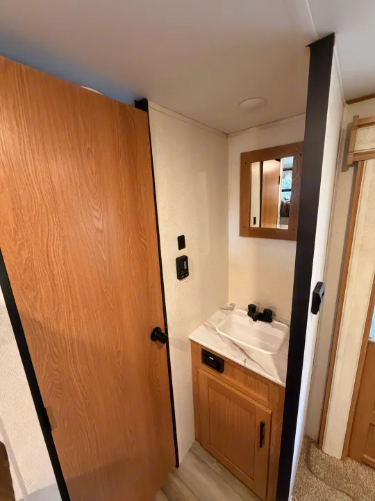RV rental bathroom featuring a modern vanity, sink, mirror, and wooden door. Light walls and control panels are visible.. Avenger LE 2022
