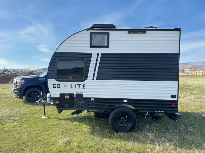 A black and white Go Lite travel trailer, ready for adventure. This RV rental is hitched to a GMC truck on a grassy field.. Wayfinder RV Go lite 2025