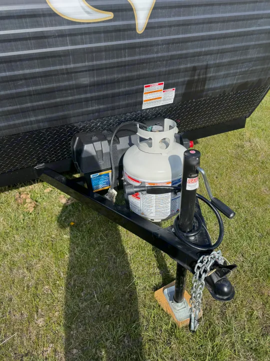 RV rental trailer's front hitch area with propane tank, CAMCO double battery box, and RAM jack on grass.. Wayfinder RV Go lite 2025