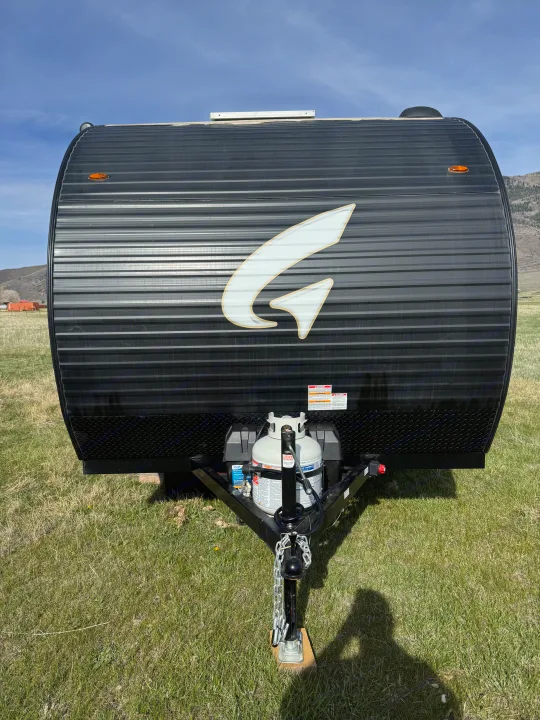 Black travel trailer (RV rental) with a white "G" logo, corrugated front, propane tank, and hitch, parked on green grass.. Wayfinder RV Go lite 2025