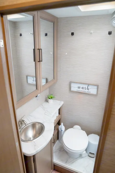 Compact and clean RV rental bathroom with a sink, toilet, mirror, and "wash your worries away" sign.. Thor Motor Coach Coleman 2023