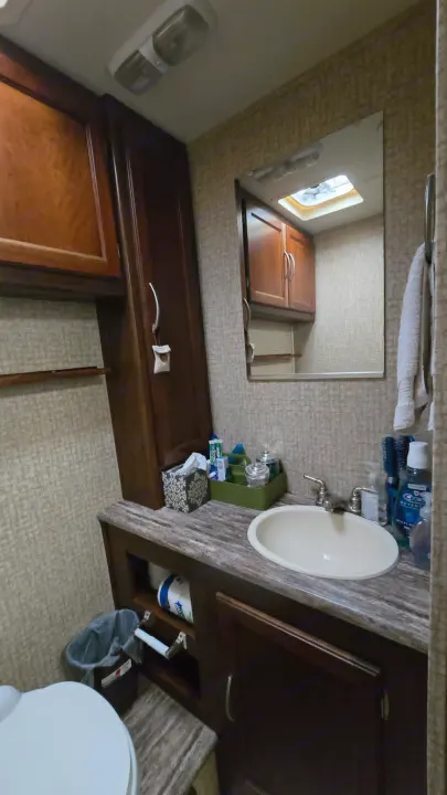 Compact RV rental bathroom: sink, mirror, toilet, and storage cabinets, efficiently designed for travel comfort.. 1F65F5DY3E0A15748 Pursuit 31 BD 2015