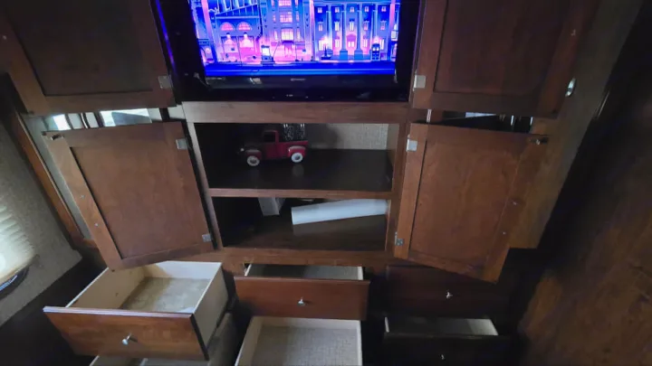 This rv rental's entertainment and storage unit features an active TV, open cabinets, and various pull-out drawers.. 1F65F5DY3E0A15748 Pursuit 31 BD 2015