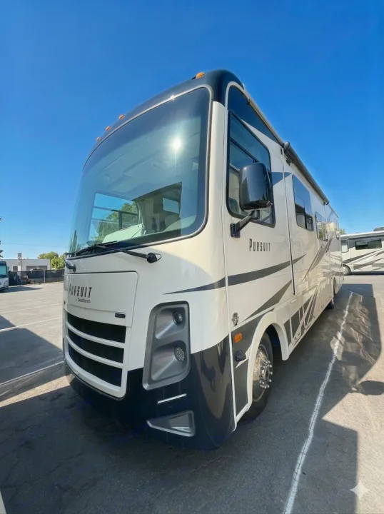 A sleek, white and black Pursuit RV rental is parked under a bright blue sky, ready for your next adventure.. Coachmen Pursuit 2019