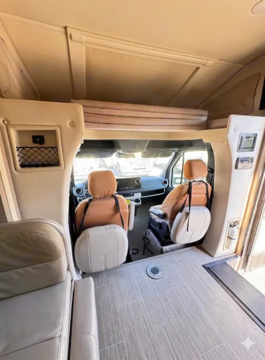 RV rental cab interior features swiveling front seats, an overhead bunk, and cream-toned living area with a tiled floor.. Thor Motor Coach Delano 2022