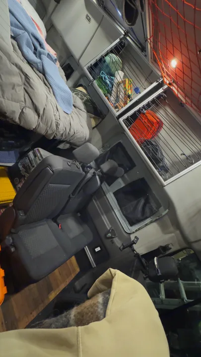 RV rental interior: cozy bed, overhead storage with gear, and vehicle seats, showcasing a compact and organized mobile living space.. Ford Custom Transit 2020