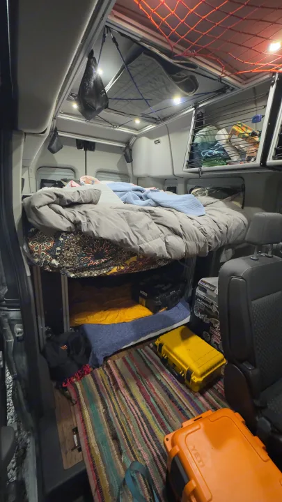 Cozy RV rental interior featuring an elevated bed, ample storage, hanging nets, and floor boxes for adventure travel.. Ford Custom Transit 2020