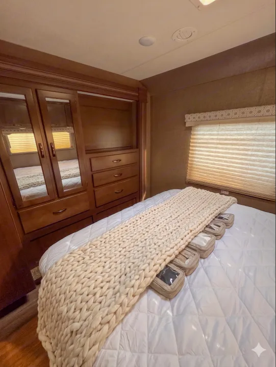 Inside an RV rental: a cozy bedroom with a bed, chunky knit cream blanket, built-in wooden wardrobe, and small travel organizers.. Thor Motor Coach 30d 2020
