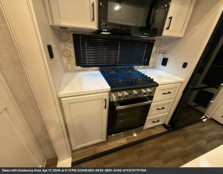 Modern RV rental kitchen: white cabinets, gas range, oven, microwave, and honeycomb backsplash. Ready for your travels!. Jayco Eagle 2025