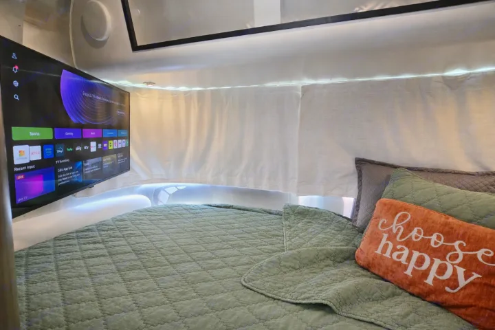 RV rental bedroom featuring a smart TV, comfy green bed with "choose happy" pillow, and warm LED lighting.. Airstream Caraval 2021