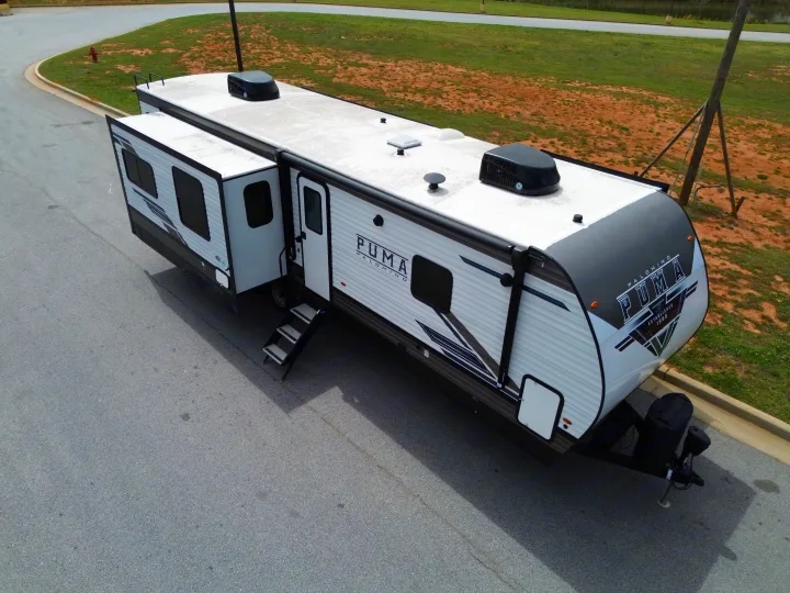 Aerial view of a white Puma Palomino travel trailer RV rental, parked on asphalt, with its slide-out and steps extended.. Forest River Puma 2023
