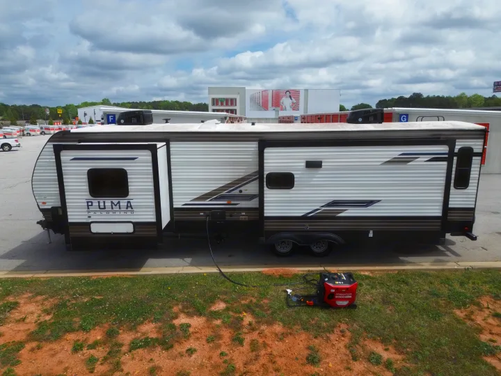 A Puma Palomino RV rental is powered by a Predator 5000 generator, parked on asphalt with storage units in the background.. Forest River Puma 2023