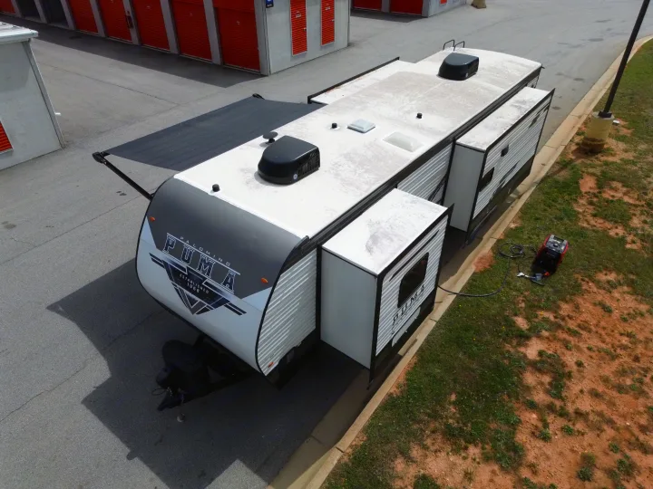 Aerial shot of a Palomino Puma travel trailer rv rental with extended slide-outs, parked by storage units, generator nearby.. Forest River Puma 2023
