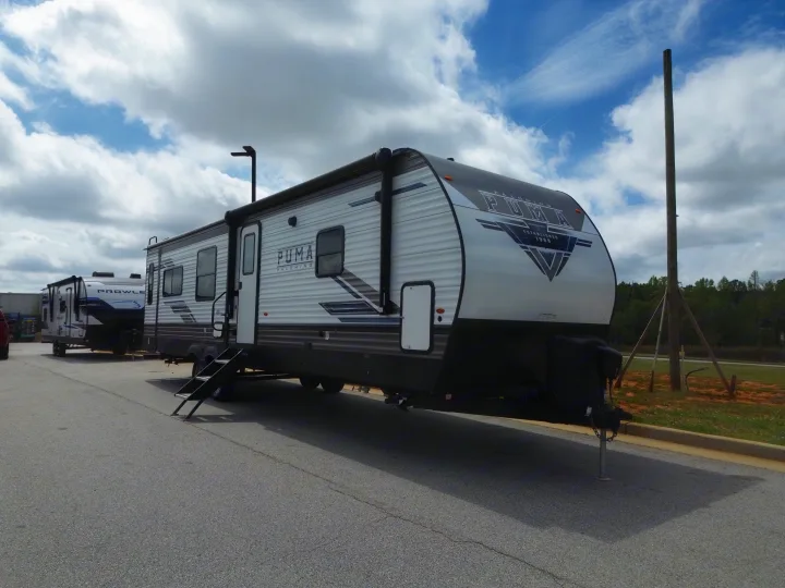 Puma Palomino travel trailer (RV rental) and another RV parked on asphalt under a cloudy sky.. Forest River Puma 2023