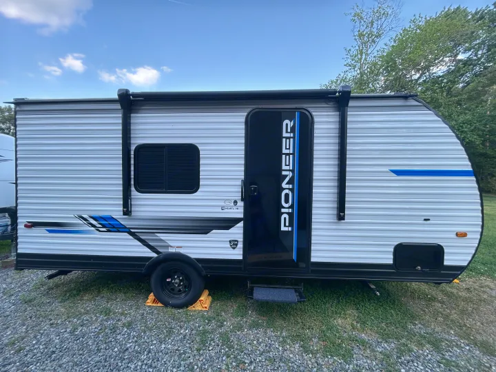 Modern Pioneer travel trailer, ideal for RV rental adventures. Side view with blue accents at a sunny campsite.. Heartland RVs Pioneer 2025